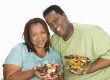 Mid-adult overweight woman and mid-adult overweight man holding bowls with fruit and vegetable salad, smiling