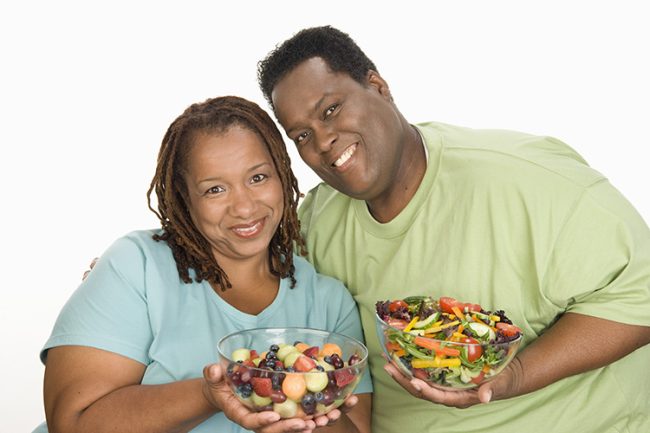 Overweight mid-adult couple Mid-adult overweight woman and mid-adult overweight man holding bowls with fruit and vegetable salad, smiling